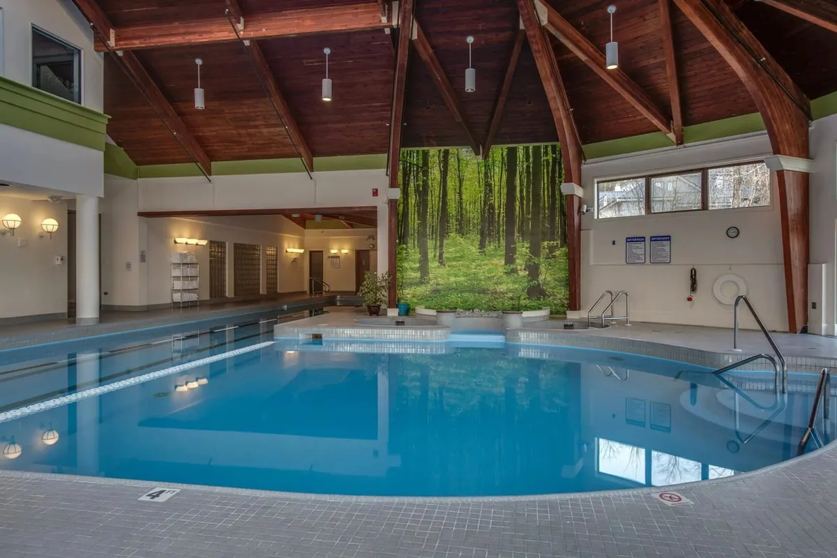 A peaceful indoor swimming pool area with a wooden ceiling, forest mural, and lush poolside plants. The space is inviting for relaxation and family bonding after outdoor winter activities.