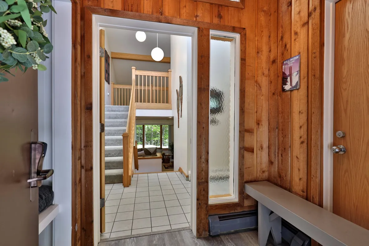 A warmly lit entryway with wooden walls, a staircase, modern light fixtures, and a welcoming bench. The decor is cozy and inviting, creating a sense of arrival and transitioning from the outside world into a private, comfortable home setting.