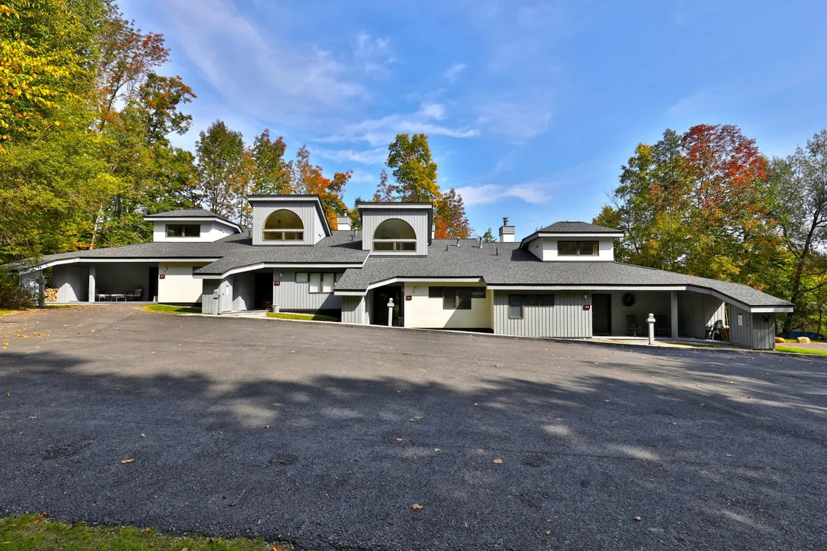 A serene exterior view showcasing unique architectural design, surrounded by trees and set against a clear blue sky. The setting suggests proximity to nature and outdoor recreation, ideal for families gathering after days spent in the snow.