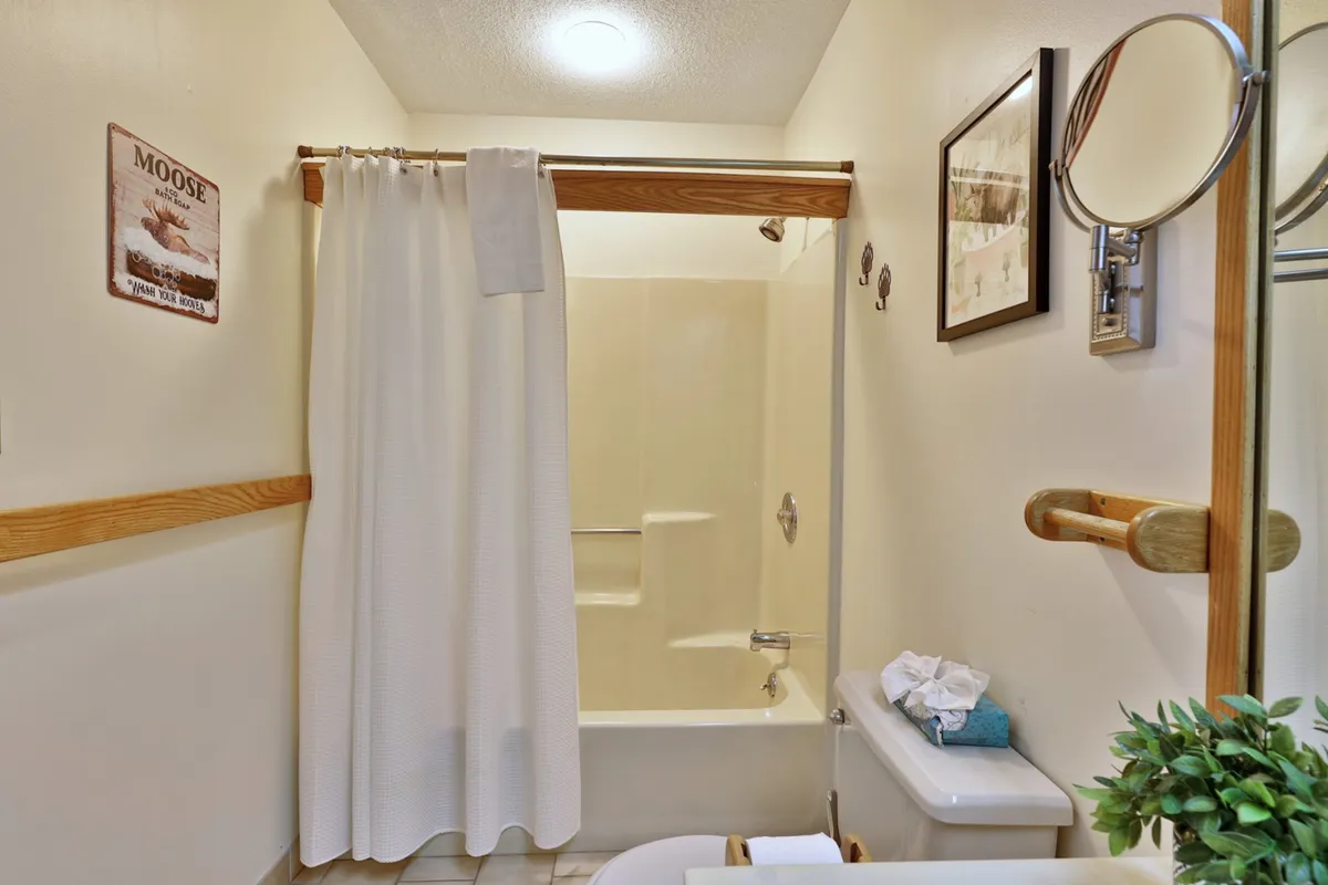 This photo depicts a clean, inviting bathroom with a bathtub, shower curtain, towel rack, and decorative elements such as framed pictures and a moose sign. The overall look is tidy and functional, aligning with the modern fixtures and refreshing spaces described.
