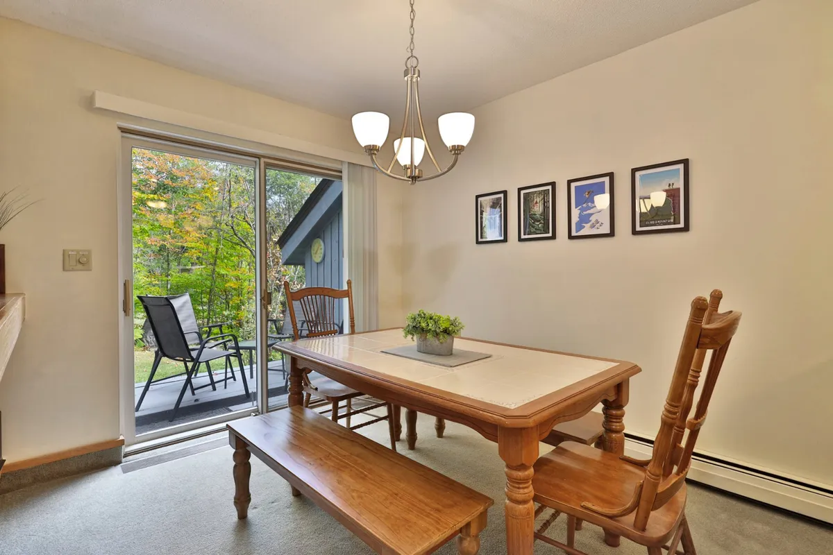 A welcoming dining area with a large table, a chandelier overhead, and sliding glass doors that open to a patio, hinting at an inviting outdoor space for gatherings. Family photos decorate the wall, reinforcing the sense of home and togetherness.