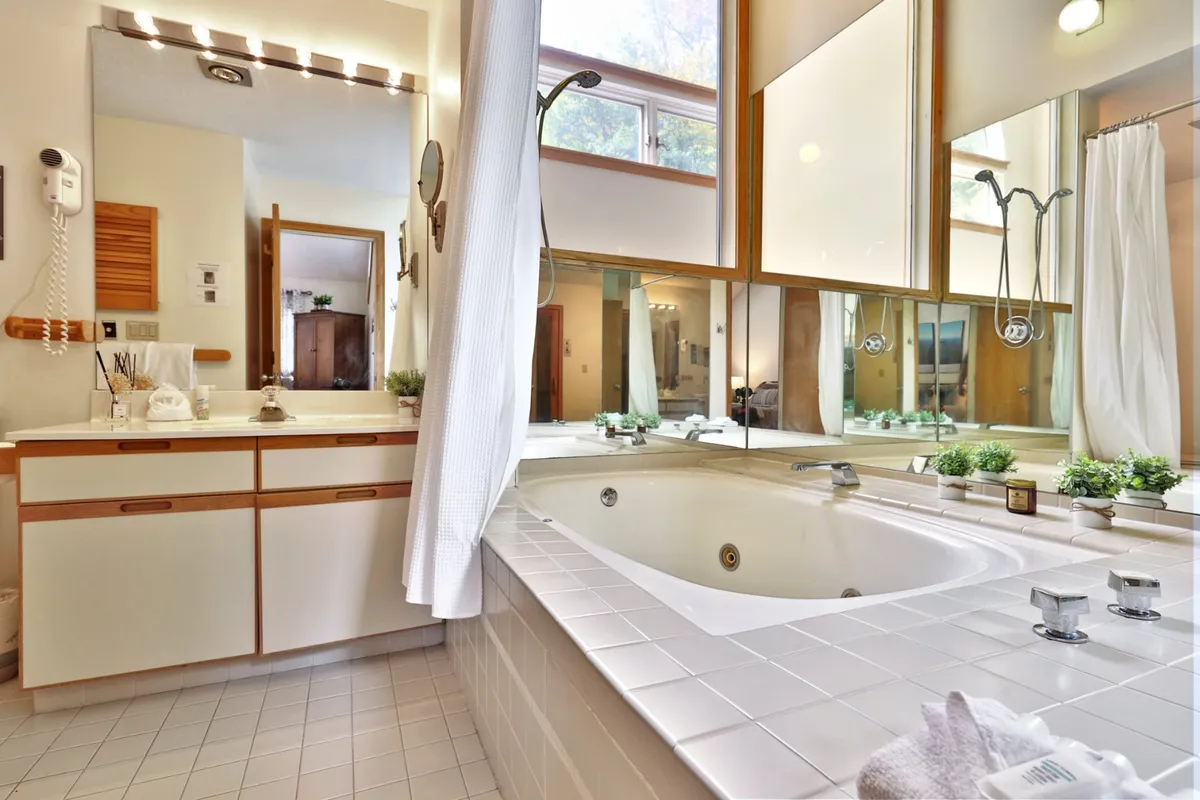 A tranquil bathroom with a deep soaking bathtub, large mirrors, and a modern sink. The ambiance is serene and soothing, evoking a spa-like experience—ideal for unwinding after a long day.