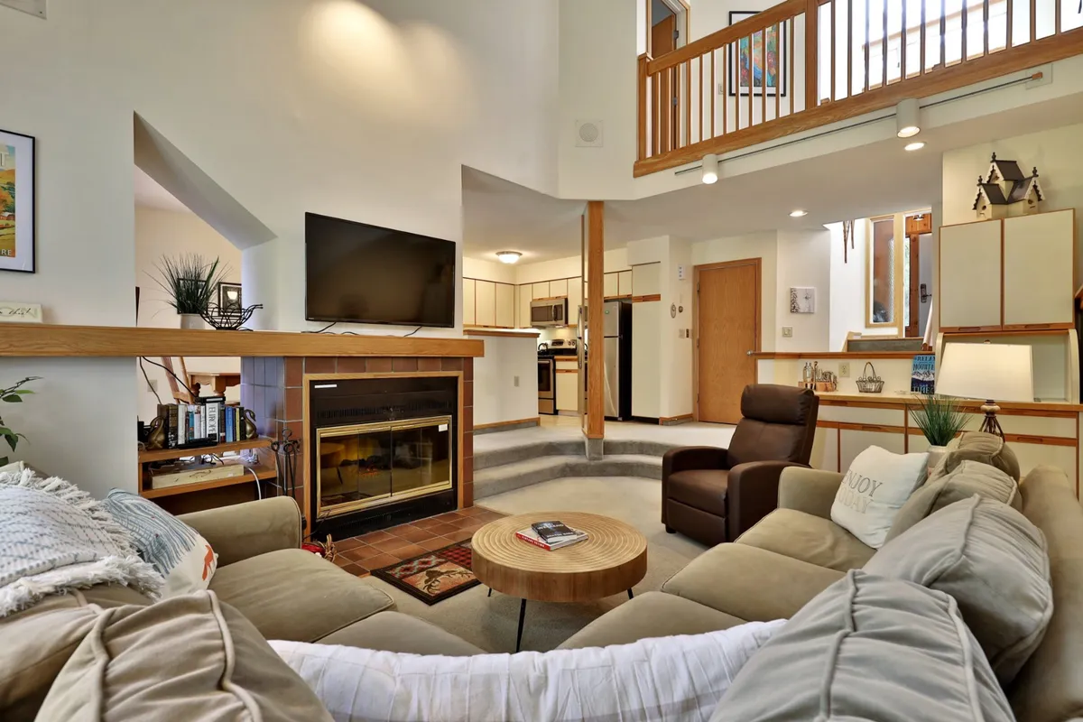 The image showcases a warm, inviting living room with a glowing fireplace as the focal point. A plush sofa seating area is arranged around a coffee table, perfect for gathering with family or friends. A television sits nearby, offering options for relaxation and entertainment. The overall atmosphere is cozy and welcoming, with soft lighting enhancing the comfortable setting.