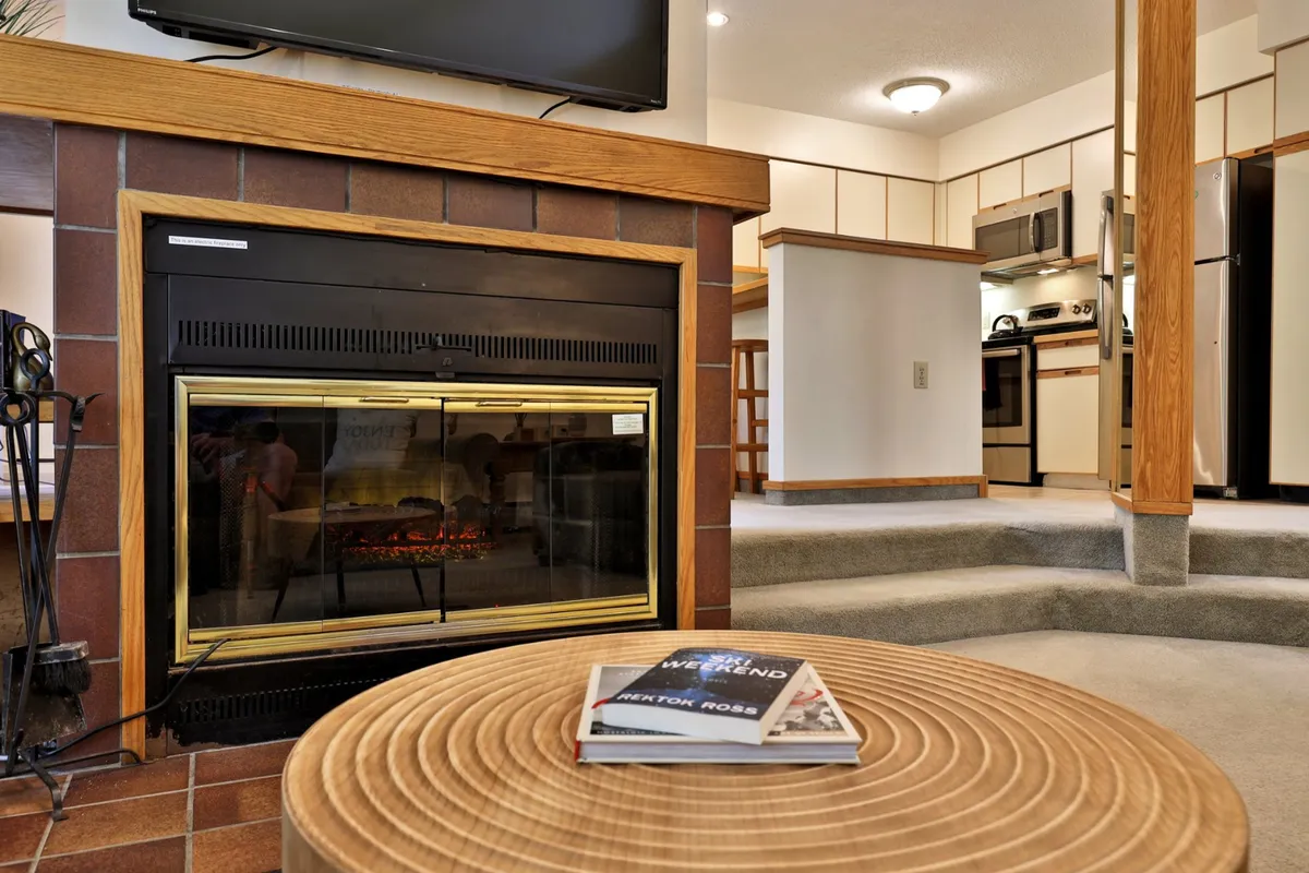A welcoming open-concept space with a fireplace, coffee table, TV, and direct view into a fully equipped kitchen area. The arrangement highlights a seamless flow between the living area and kitchen, inviting group activities like movie nights or shared meals.