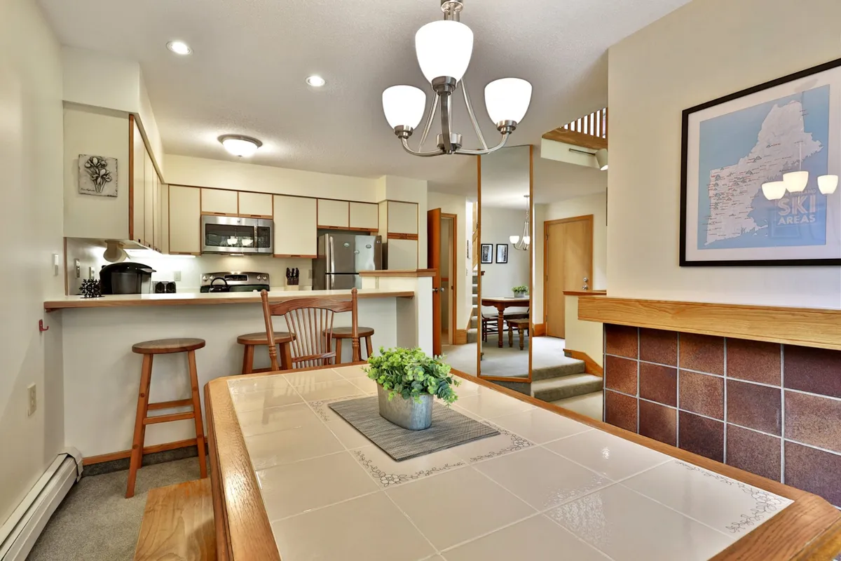 A spacious dining area with a large table, kitchen counter, stylish lighting, and inviting wall art. The setup suggests an ideal space for shared meals, celebrations, and casual gatherings with family or friends.