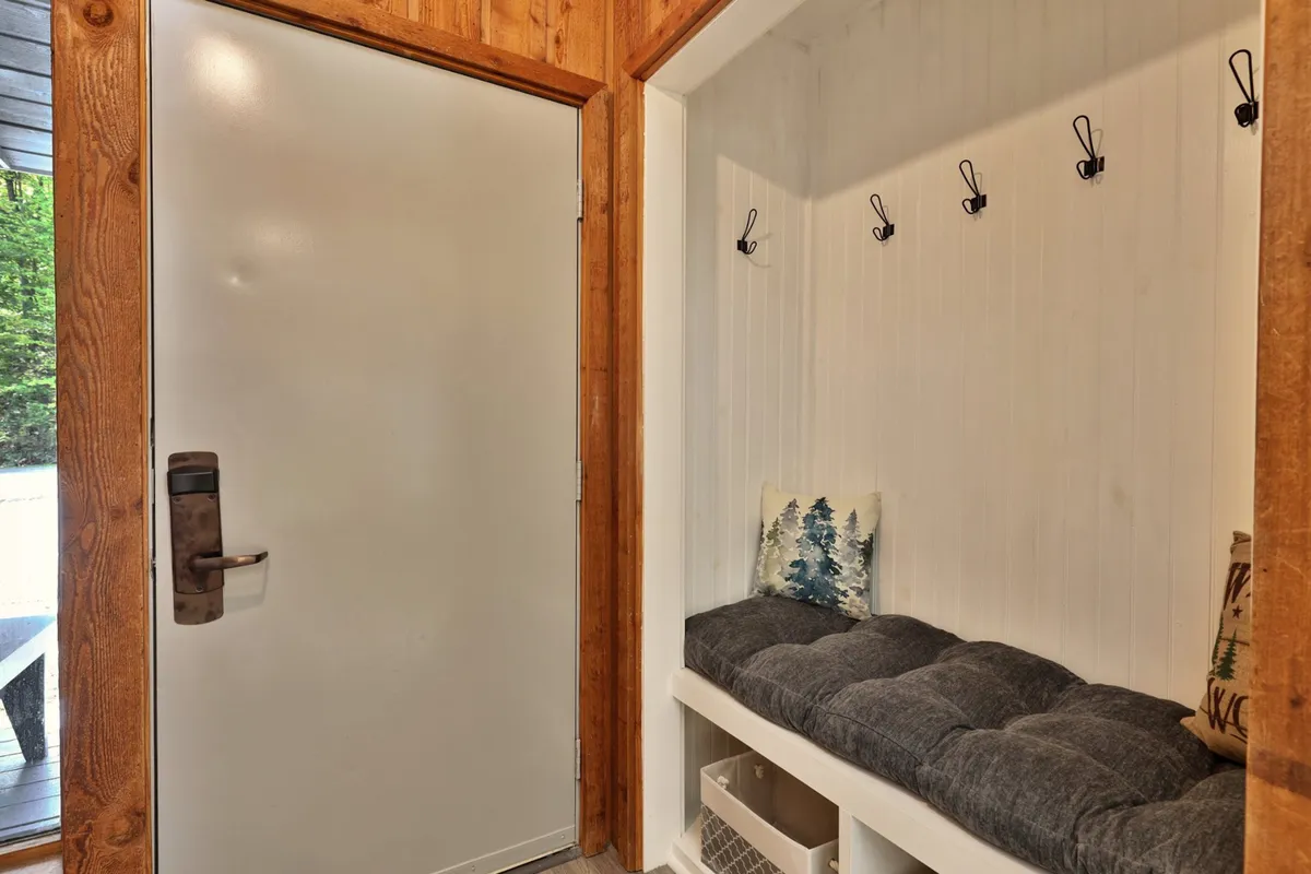 A bright and inviting entryway with a front door opening to the outside, bench seating, hooks for gear, and a decorative pillow. The setup makes it easy to transition from outdoor adventure to indoor comfort.