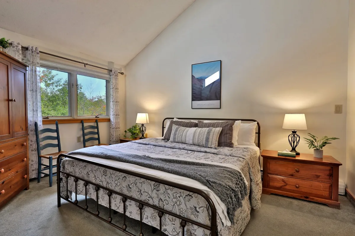 This image features a serene bedroom with a large bed (likely a king-sized bed), nightstands, a window that lets in natural light, a chair, and tasteful artwork. The space feels inviting, spacious, and restful, echoing the description of a master bedroom designed for restorative sleep.