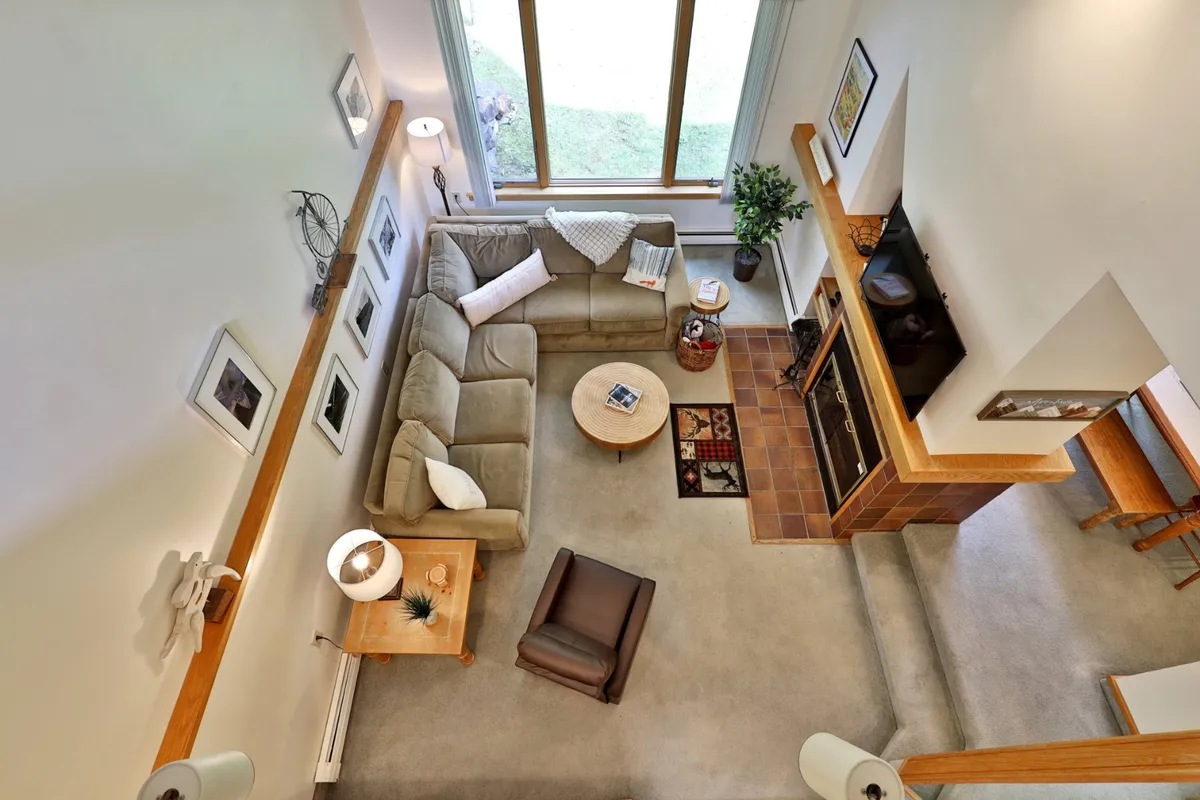 A cozy living room featuring a corner sectional sofa arranged around a wood-burning fireplace, with a coffee table in the center and large windows letting in abundant natural light. The space exudes warmth and comfort, perfect for relaxing, reading, or socializing after a day outdoors.
